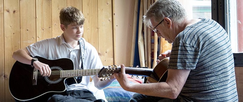 Ein Betreuer übt mit einem Jungen Gitarre zu spielen
